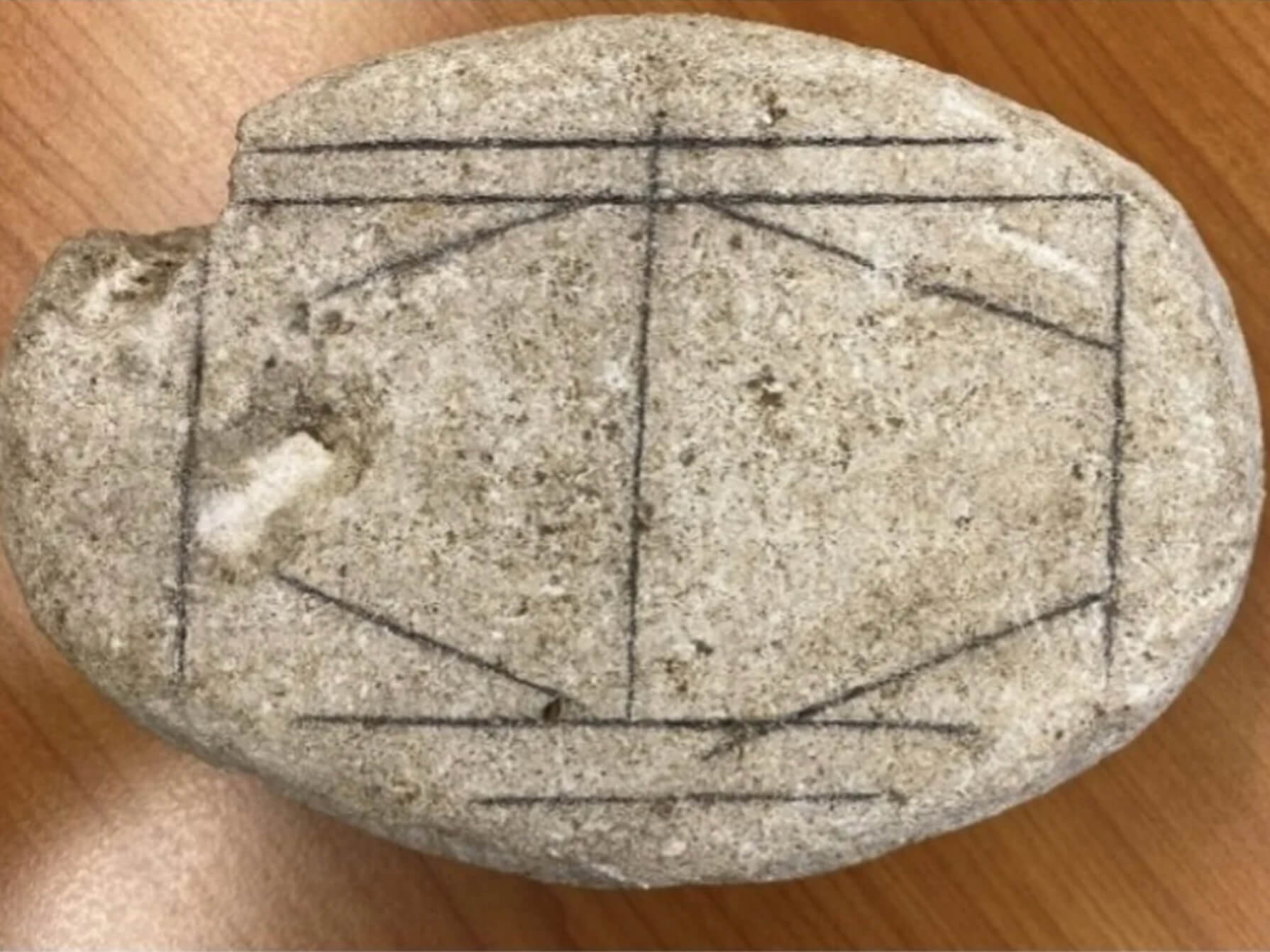 Photo of a stone, a possible game board, with pencil marks highlighting the incised lines.