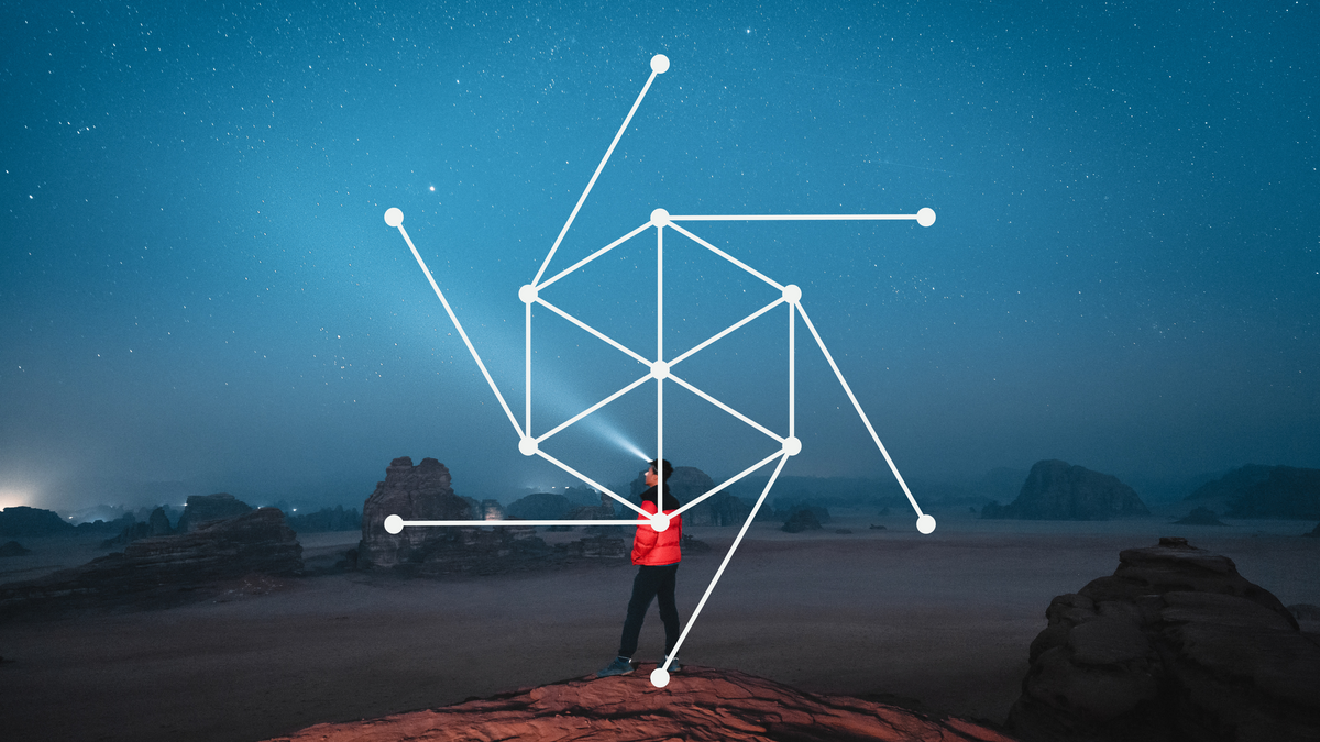 Man standing on a mountain in a desert landscape looking at the night sky.