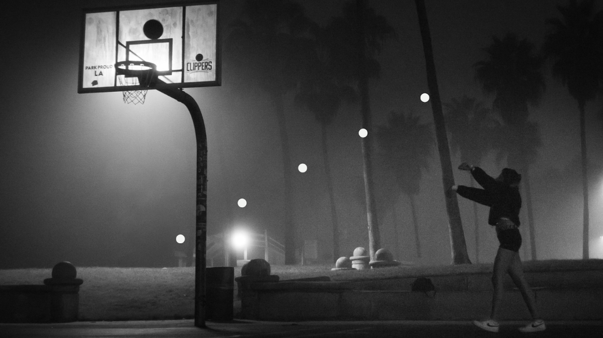 Black and white photo of a person shooting a basketball. the ball hovers just above the hoop.