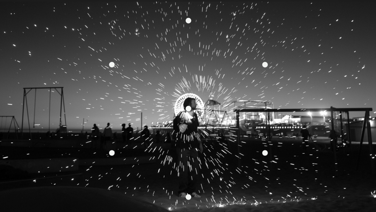 Black and white photo of a man at the beach at night with sparks encircling his head.